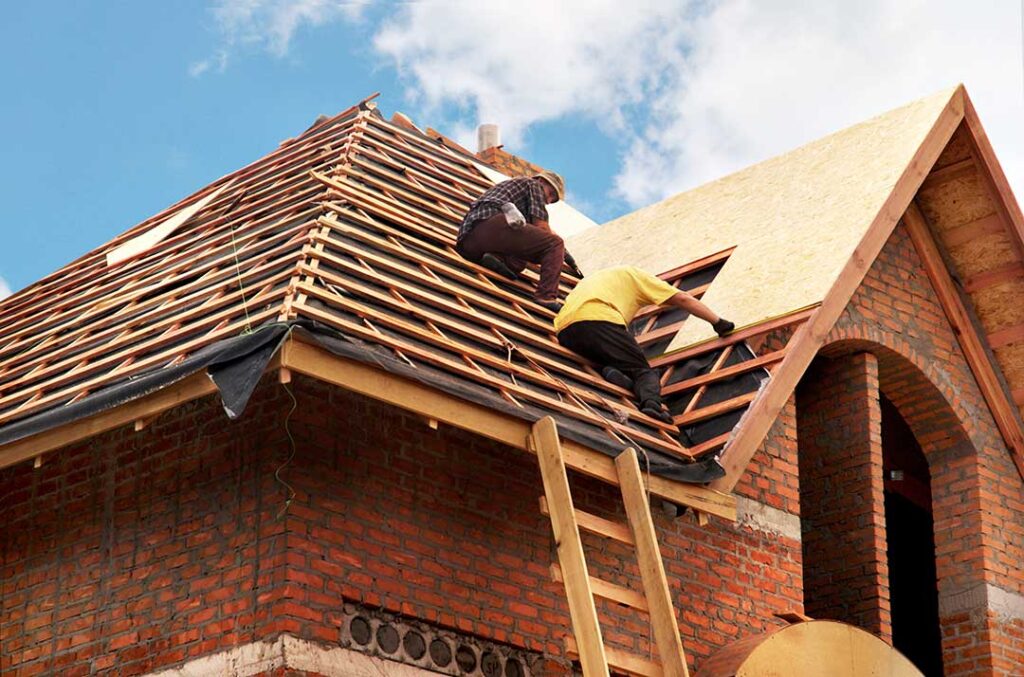 Roofing workers repair a damaged shingle area while a resident observes from a safe distance outdoors.