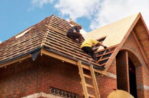 Roofing workers repair a damaged shingle area while a resident observes from a safe distance outdoors.